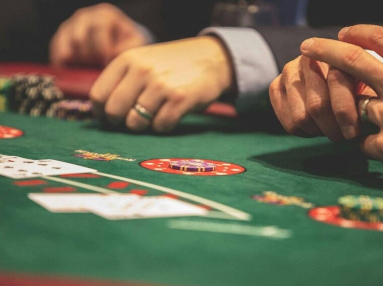 A close-up of players’ hands, poker chips, and cards on a green casino table.